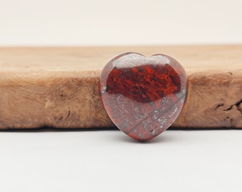 May include: A heart-shaped red jasper stone with a polished finish. The stone has a deep red color with white and gray veins running through it.