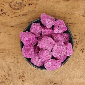 May include: A black bowl filled with pink, irregularly shaped, dried fruit pieces.