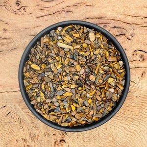 May include: A black bowl filled with small, golden brown tiger's eye stones. The bowl is sitting on a wooden surface.