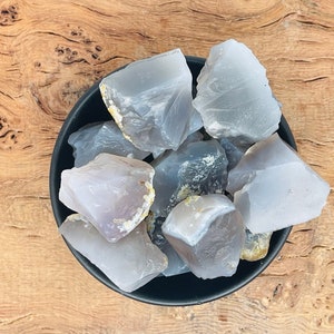 May include: A collection of gray and white agate crystal chunks in a black bowl. The crystals have a smooth, polished surface and are arranged in a random pattern.