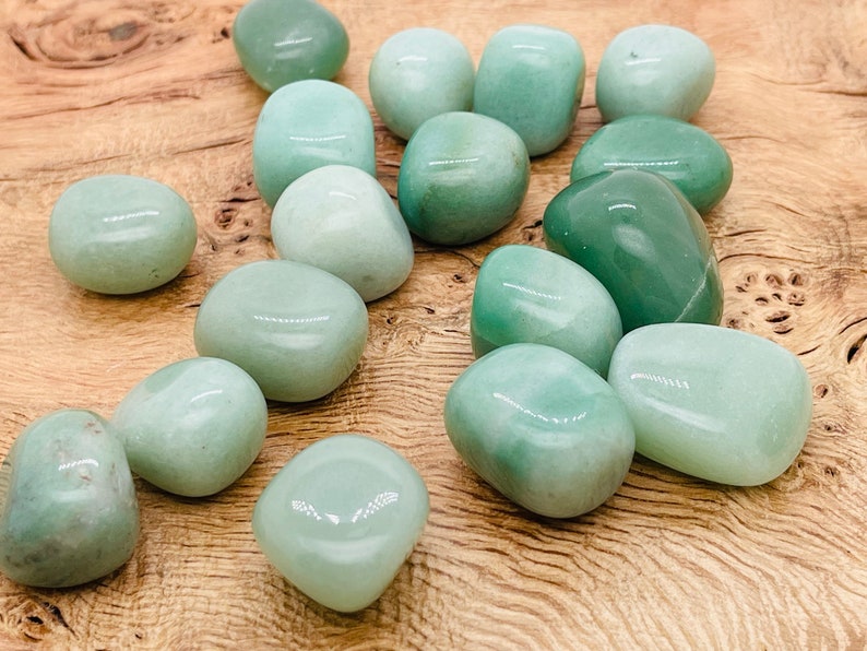 May include: A collection of smooth, light green tumbled stones. The stones are various sizes and shapes, and have a polished, glossy finish.