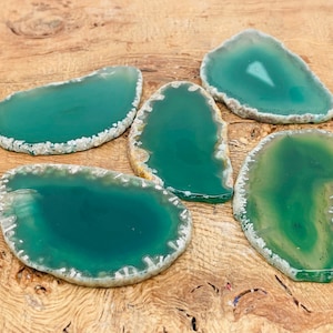 Könnte beinhalten: Fünf grüne Achat-Scheiben mit weißen Rändern. Die Achat-Scheiben sind glatt und poliert und haben eine natürliche, organische Form.