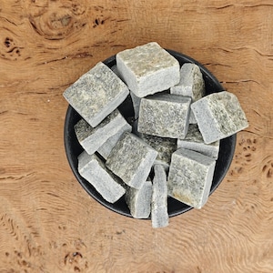 May include: A bowl filled with small, gray and green tumbled stones. The stones are smooth and have a natural, rustic look.
