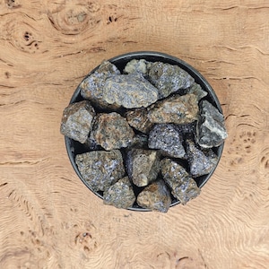 Könnte beinhalten: Eine schwarze Schale gefüllt mit dunkelgrauen und braunen, grob geschnittenen Steinen.