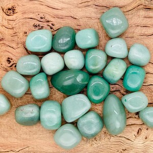 May include: A collection of smooth, green tumbled stones. The stones are various shades of green and are arranged in a pile on a wooden surface.