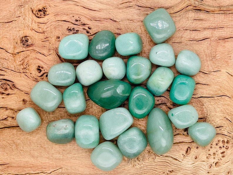May include: A collection of smooth, green tumbled stones. The stones are various shades of green and are arranged in a pile on a wooden surface.