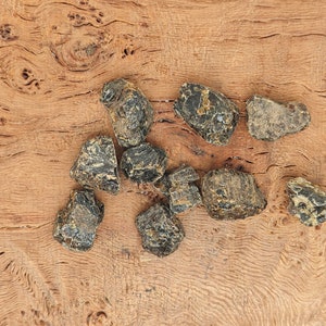 May include: A collection of nine black and brown rough, irregular shaped stones on a wooden surface.