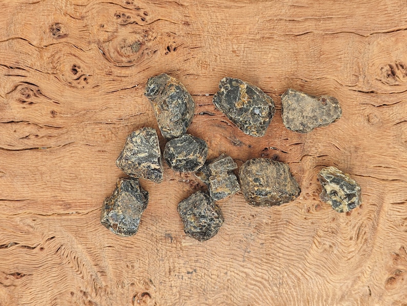 May include: A collection of nine black and brown rough, irregular shaped stones on a wooden surface.