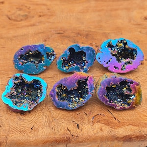 May include: Six iridescent crystal geodes with a purple, blue and gold colour scheme. The geodes are arranged in a semi-circle on a wooden surface.