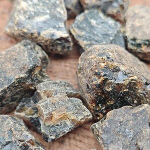 May include: A collection of dark amber stones with a variety of shapes and sizes. The stones have a rough, natural texture and a deep, rich color.