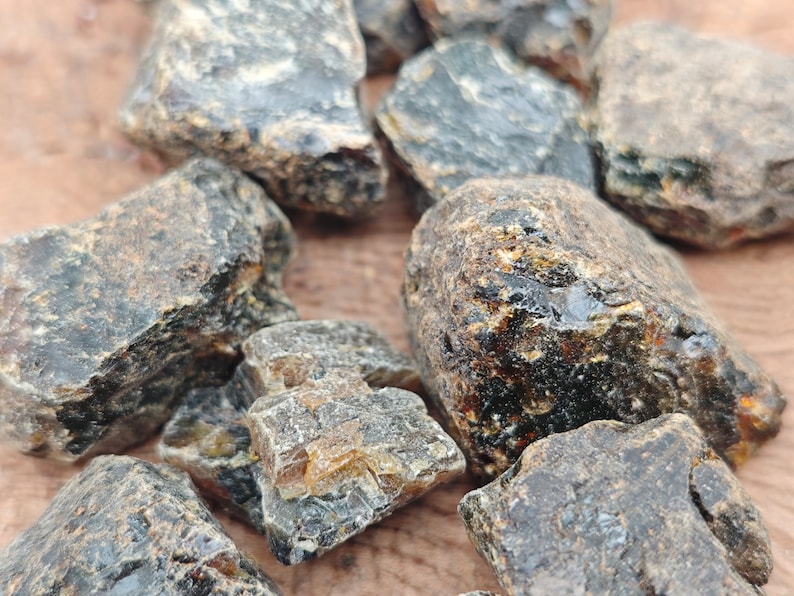 May include: A collection of dark amber stones with a variety of shapes and sizes. The stones have a rough, natural texture and a deep, rich color.