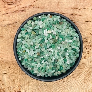 May include: A black bowl filled with small, light green and clear tumbled stones. The bowl is sitting on a wooden surface.