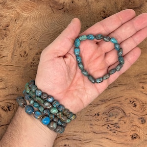 May include: A bracelet made of blue and brown oval-shaped beads. The bracelet is on a person's wrist.