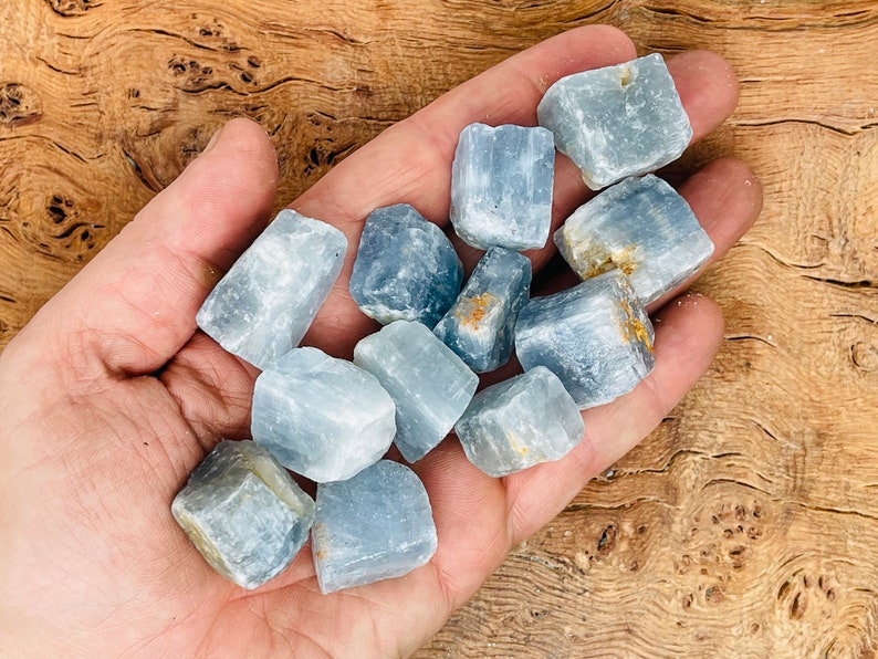May include: A collection of blue celestite crystals, each with a unique shape and size. The crystals are smooth and have a light blue color.