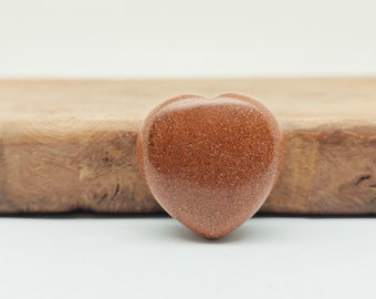 May include: A heart-shaped, polished, brown sandstone crystal with a glittery texture.