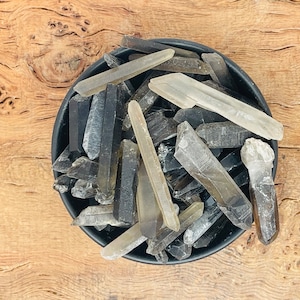 Può includere: Una ciotola nera piena di punte di cristallo di quarzo fumè e quarzo chiaro.