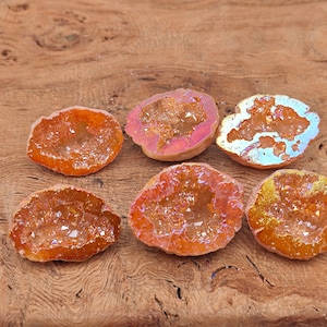May include: Six orange agate geode slices with iridescent interiors. The geode slices are arranged in a row on a wooden surface.