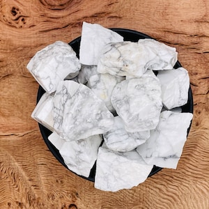 May include: A bowl filled with white and grey tumbled Howlite stones. The stones are rough and have a natural, organic look.