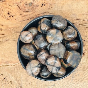 May include: A black bowl filled with tumbled brown and black stones. The stones have a unique cross-hatch pattern.