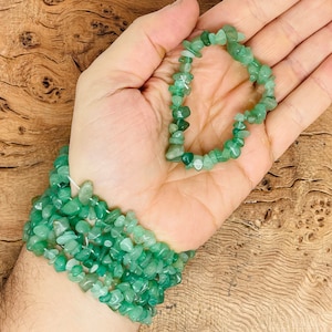 Puede incluir: Un brazalete de chips de piedras preciosas verdes con una hebra de las mismas chips envuelta alrededor de una muñeca.