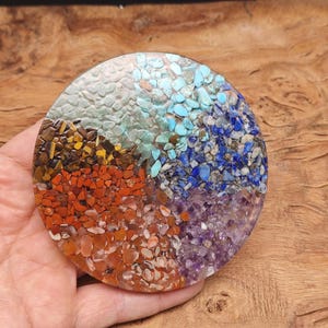 May include: Round resin coaster with embedded gemstones in a circular pattern. The coaster features five colours of gemstones: turquoise, blue, purple, orange, and brown.