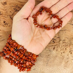 May include: A red gemstone chip bracelet with multiple strands. The bracelet is made of small, irregular shaped chips of red jasper.