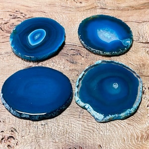 May include: Four blue agate coasters with natural edges. The coasters are round and have a polished surface. The agate has a white and blue pattern.