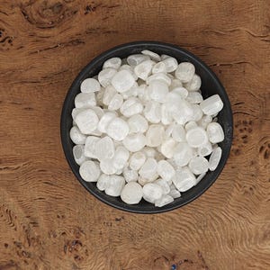 May include: A black bowl filled with white tumbled selenite stones. The bowl is sitting on a wooden surface.