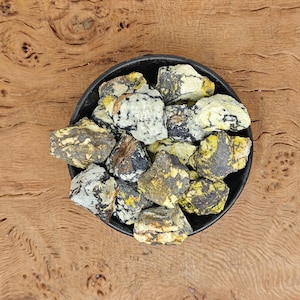 Może przedstawiać: Miska z żółtymi, czarnymi i białymi kamieniami mineralnymi. Kamienie są szorstkie i mają naturalny, nieoszlifowany wygląd.