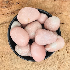 Può includere: Una ciotola nera piena di pietre lisce, rosa e bianche. Le pietre sono di diverse dimensioni e forme.
