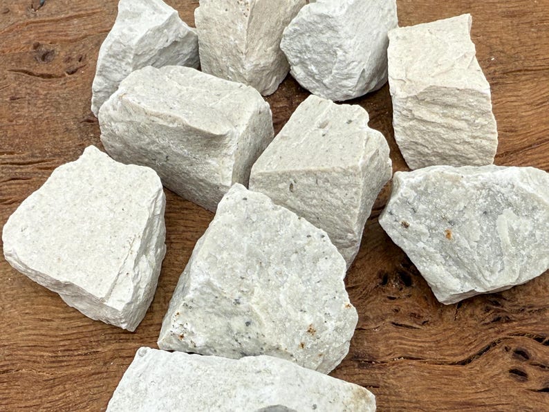 Puede incluir: Un conjunto de piedras de color gris claro, de forma irregular y con superficie rugosa y texturizada. Las piedras son de diferentes tama&ntilde;os y est&aacute;n dispuestas sobre una superficie de madera, creando una est&eacute;tica natural y terrosa. Ideal para manualidades o decoraci&oacute;n.