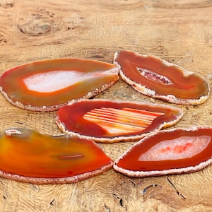 May include: Four agate slices in shades of orange, red, and brown with white and clear quartz inclusions. The agate slices are arranged on a wooden surface.