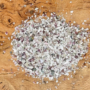 May include: A close-up of a pile of small, white and pink, iridescent, natural gemstone chips on a wooden surface.