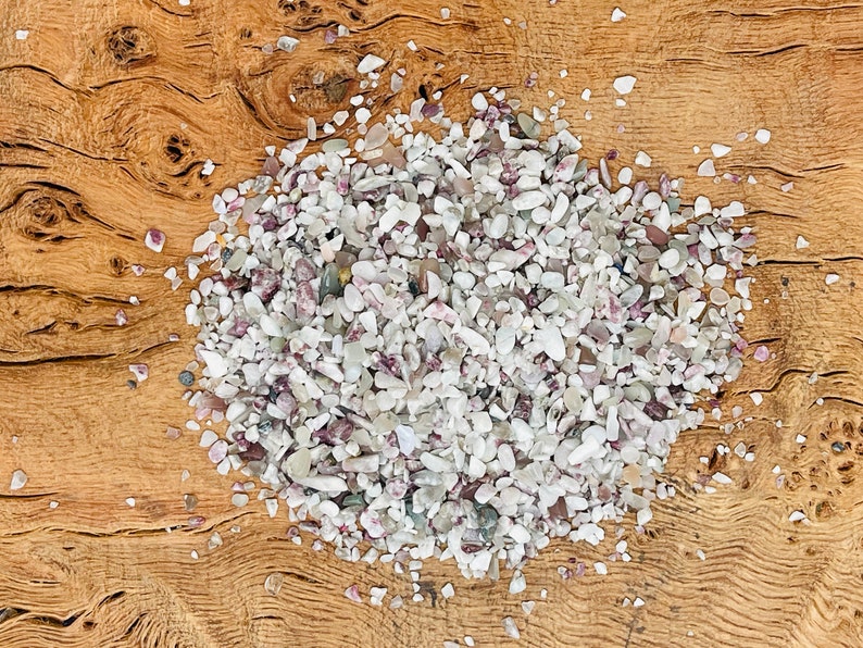 May include: A close-up of a pile of small, white and pink, iridescent, natural gemstone chips on a wooden surface.