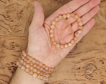 May include: A stack of bracelets made with light orange and white gemstone beads. The bracelets are on a person's wrist.