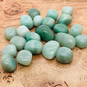 May include: A collection of smooth, green aventurine tumbled stones. The stones are various sizes and shapes, and have a polished, glassy finish.