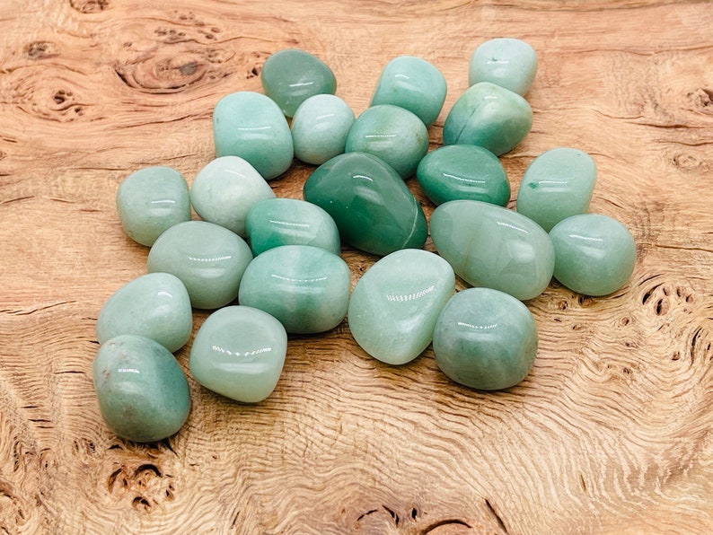 May include: A collection of smooth, green aventurine tumbled stones. The stones are various sizes and shapes, and have a polished, glassy finish.