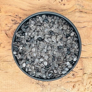 Puede incluir: Un cuenco negro lleno de pequeñas piedras pulidas transparentes y negras. Las piedras son lisas y pulidas.