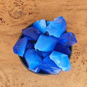 May include: A small black bowl filled with blue glass shards. The bowl is sitting on a wooden surface.