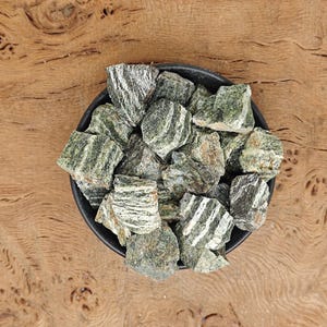 May include: A bowl filled with green and white striped stones. The stones are in a black bowl and are on a wooden surface.