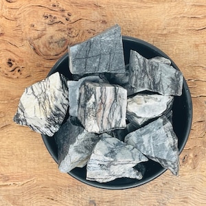 Puede incluir: Un cuenco negro lleno de piedras rugosas rayadas de gris y blanco. El cuenco está sobre una superficie de madera.