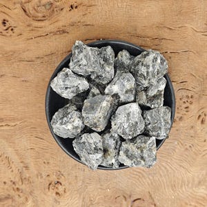 Könnte beinhalten: Eine schwarze Schale gefüllt mit einer Sammlung grauer und schwarzer Steine. Die Steine sind rau und haben ein natürliches, unpoliertes Aussehen.