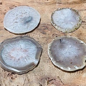 May include: Four agate coasters in various shades of grey and white. The coasters are round and have a natural, polished finish.