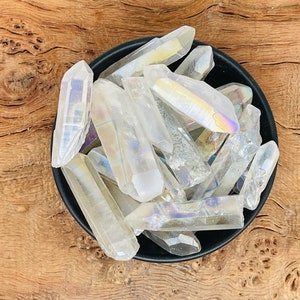 Puede incluir: Un bol lleno de puntas de cristal de cuarzo claro iridiscente. Los cristales son de varios tamaños y formas, con un brillo arcoíris.