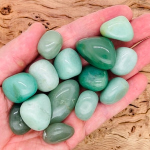 May include: A collection of smooth, green tumbled stones, likely jade or aventurine, in a hand. The stones are various shades of green, from light to dark.