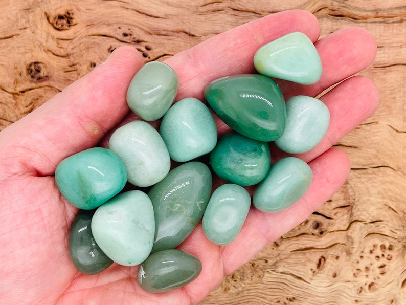 May include: A collection of smooth, green tumbled stones, likely jade or aventurine, in a hand. The stones are various shades of green, from light to dark.