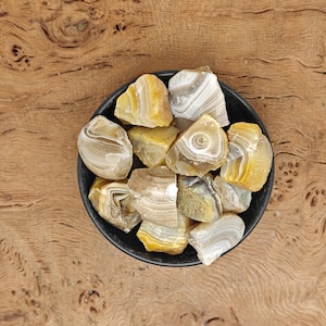 Puede incluir: Un cuenco de piedras de ágata amarillas y blancas. Las piedras son ásperas y tienen una forma natural y orgánica.