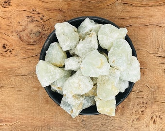 Puede incluir: Un cuenco negro lleno de trozos de resina de incienso crudo blanco y verde.