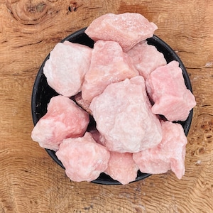 May include: A black bowl filled with pink rose quartz crystals. The crystals are rough and have a natural, unpolished look.