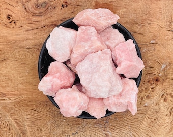 May include: A black bowl filled with pink rose quartz crystals. The crystals are rough and have a natural, unpolished look.